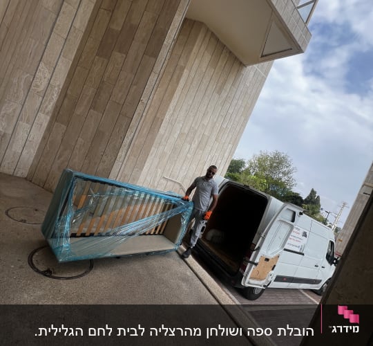 אדם מעביר מיטה עטופה ליד רכב מסחרי לבן